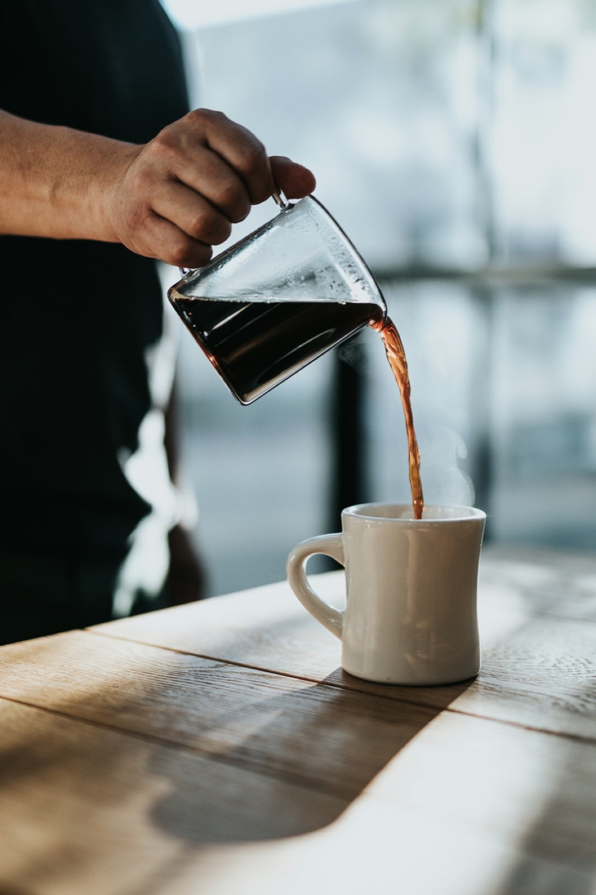 Coffee being poured into a white ceramic mug on a wooden table.