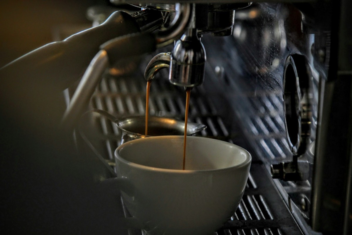 Espresso dripping from a steel machine into a porcelain mug.