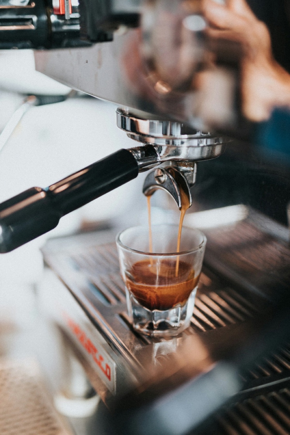 Espresso pouring into a clear glass from a silver coffee machine.