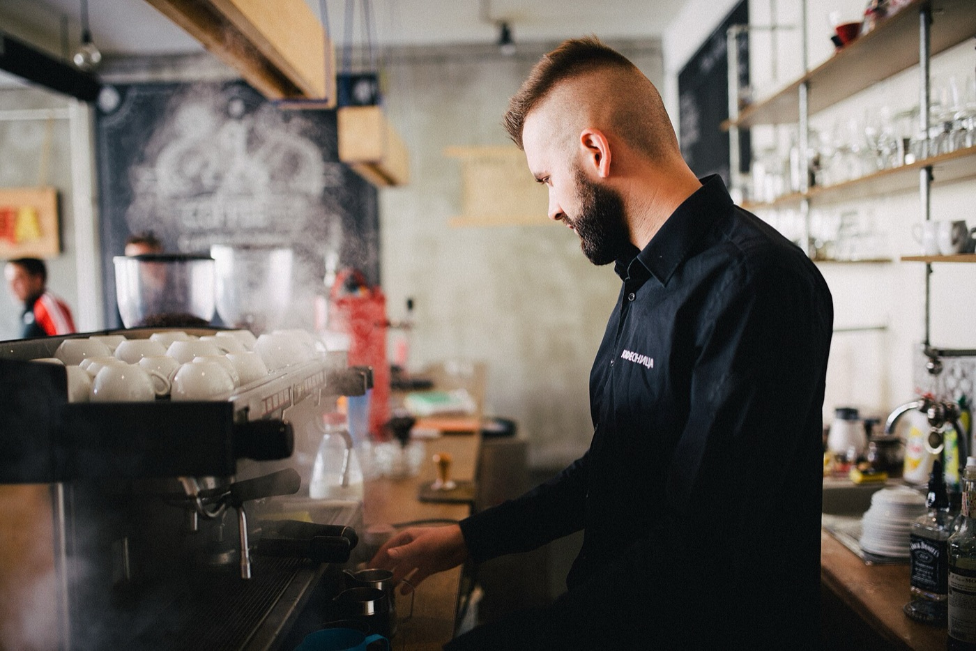A barista working beside a steaming espresso machine.